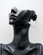 Mannequin head wearing a silver floral earring on a light gray background