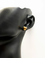 Gold earring on a black mannequin ear against a white background