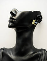 Black mannequin head wearing gold hoop earrings on a white background