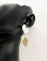 Gold and white leaf-shaped earrings on a black mannequin ear.