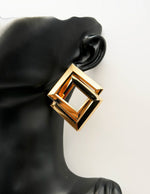 Gold geometric earring on a black mannequin ear against a white background