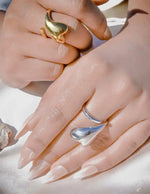 Close-up of hands wearing gold and silver rings on a light background