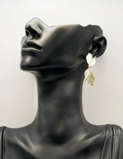 Mannequin head wearing a gold and white leaf-shaped earring on a plain background