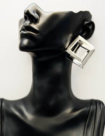 Black mannequin head with a silver square earring on a white background