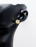 Gold earring on a black mannequin ear against a white background
