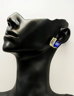 Sparkling sapphire blue and gold earrings resting on a vintage-style display.