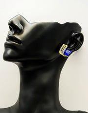 Sparkling sapphire blue and gold earrings resting on a vintage-style display.