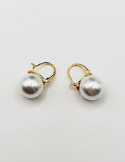 Biya Accessoires gold huggie hoop earrings with large white pearl drop.