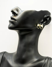 Black mannequin head with a gold bow-shaped earring on a white background