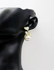 Close up of elegant imitation jewelry uae featuring a pavé crystal heart, gold bow, and faux pearl drop.