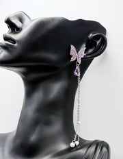 Close up of imitation jewelry uae statement earrings featuring purple rhinestone wings and pearls.
