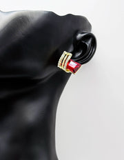 Gold and red earring on a black mannequin ear against a white background
