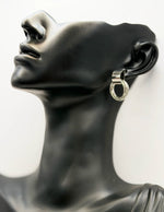 Mannequin head wearing a silver hoop earring with black stones on a white background