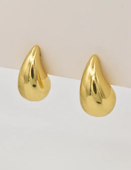 Gold teardrop earrings resting on a neutral background