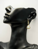 Gold earring on a black mannequin head with a white background