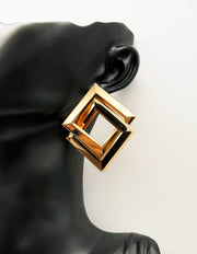 Gold geometric earring on a black mannequin ear against a white background