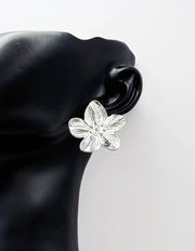 Silver flower-shaped earring on a black mannequin ear against a white background