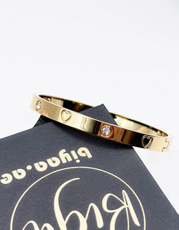 Gold bracelet with heart and diamond design on a Pying & Co branded card.