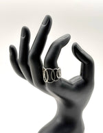 Black mannequin hand wearing a silver ring with three circular designs on a white background