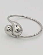 Silver bangle with two teardrop-shaped charms on a light gray background