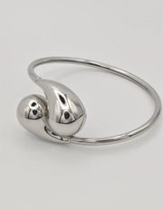 Silver bangle with two teardrop-shaped charms on a light gray background