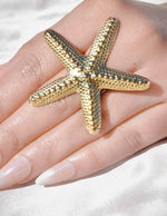 Gold starfish ring on a hand with a white background
