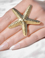 Gold starfish ring on a hand with a white background