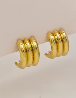 Triple gold conch earrings displayed on soft beige card